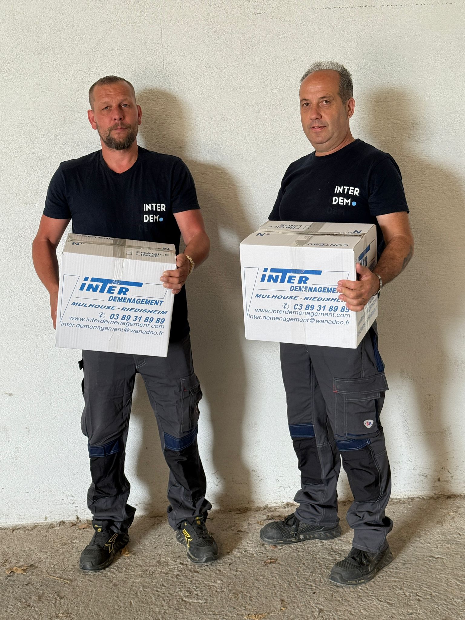 Deux déménageurs en uniforme Inter Déménagement portant chacun un carton lors d’un déménagement