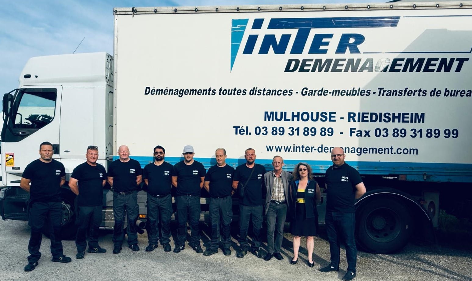 Photo de groupe de l’équipe Inter Déménagement réunie devant un mur clair, représentant une entreprise familiale et professionnelle basée en Alsace.