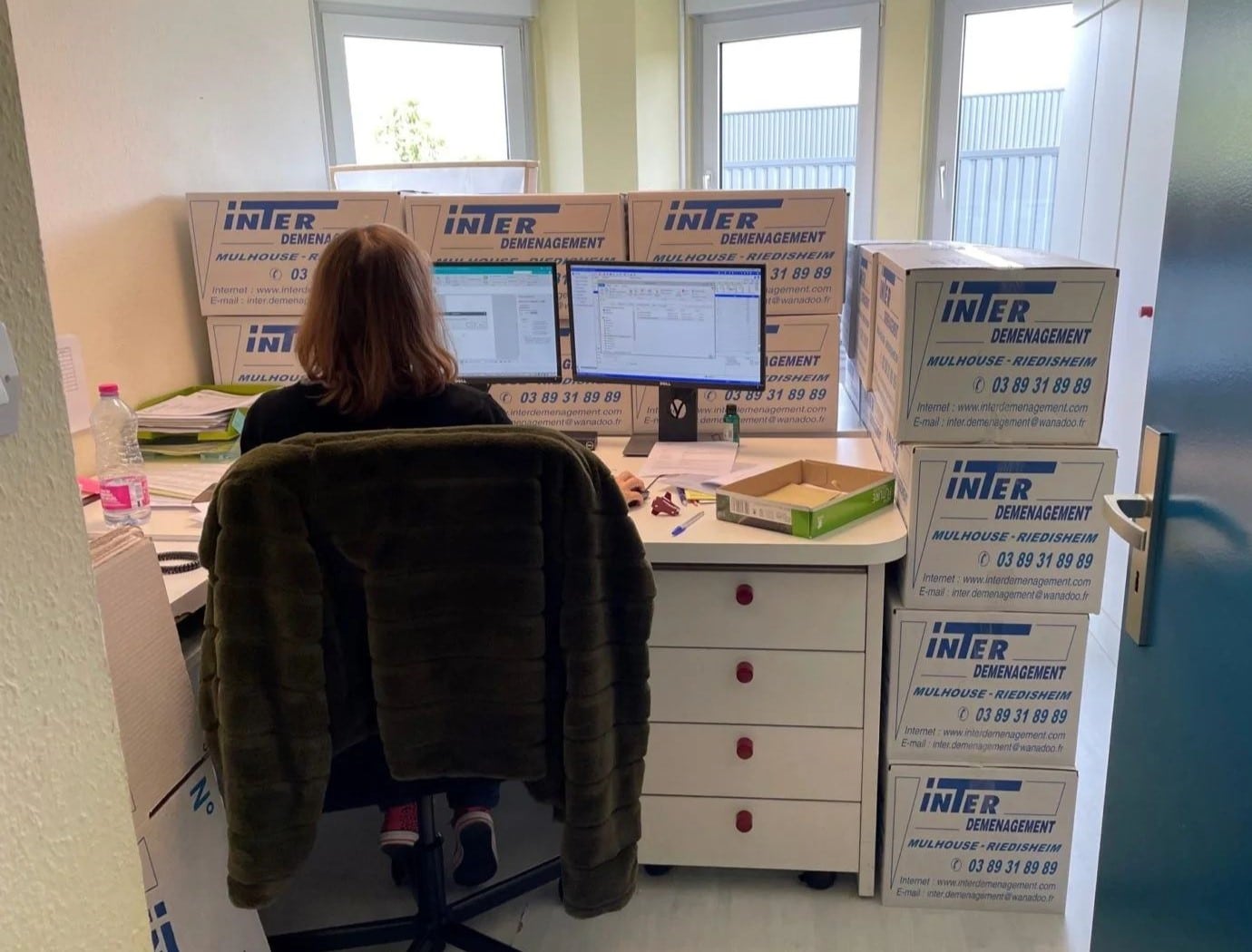 Bureau d’une femme entouré de cartons de déménagement pendant le transfert d’un espace de travail.