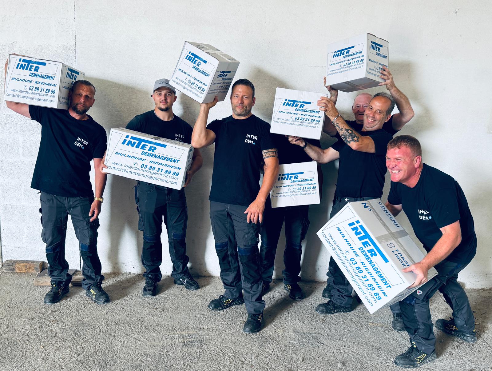 Équipe souriante d’Inter Déménagement tenant des cartons personnalisés, illustrant la bonne ambiance et le professionnalisme de l’entreprise de déménagement basée à Mulhouse.